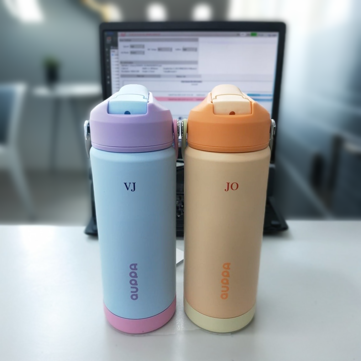Two quppa custom insulated water bottles with colored lids on a desk in an office setting.